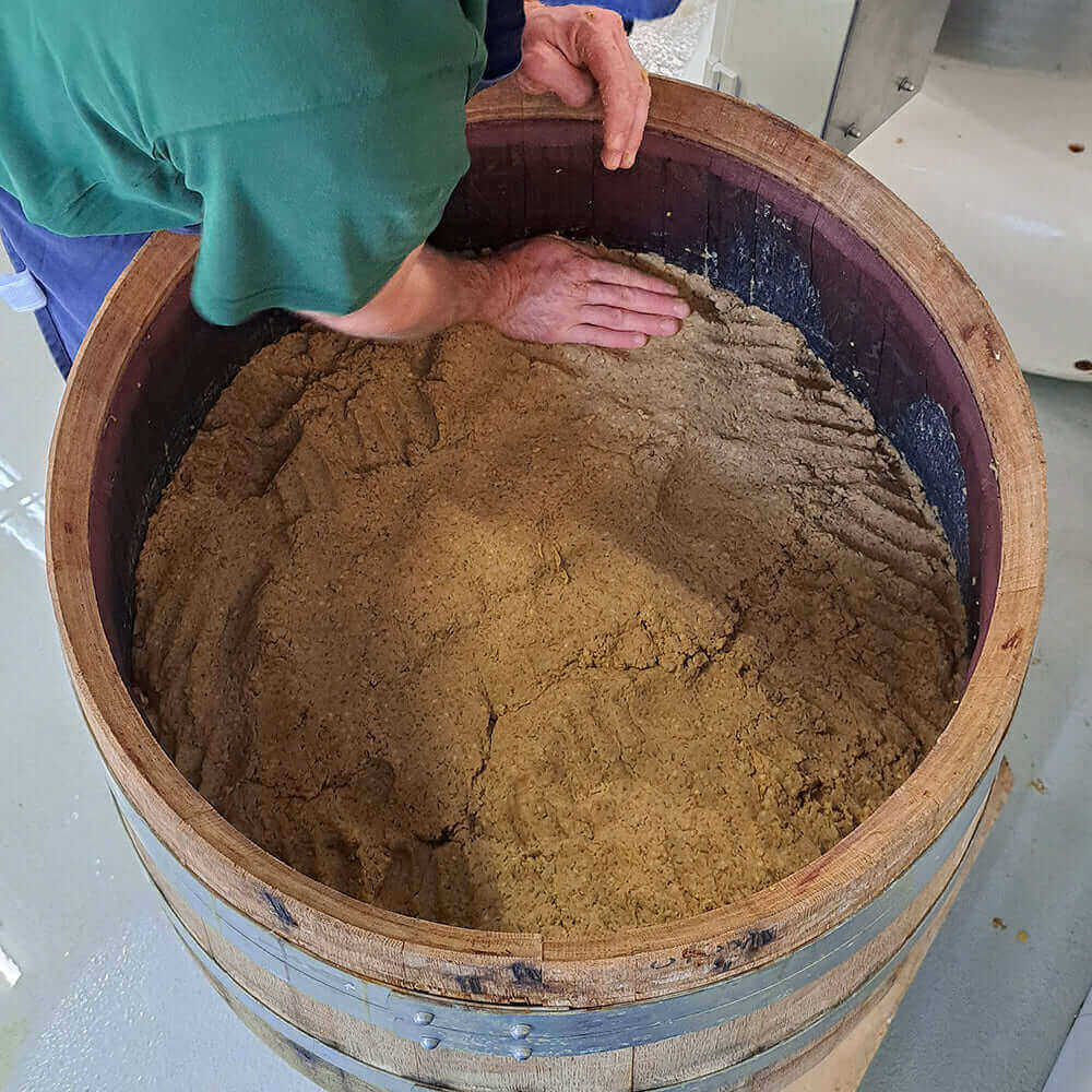 Ein Handwerker bearbeitet frisch zubereitete Miso Paste in einem Holzfass.