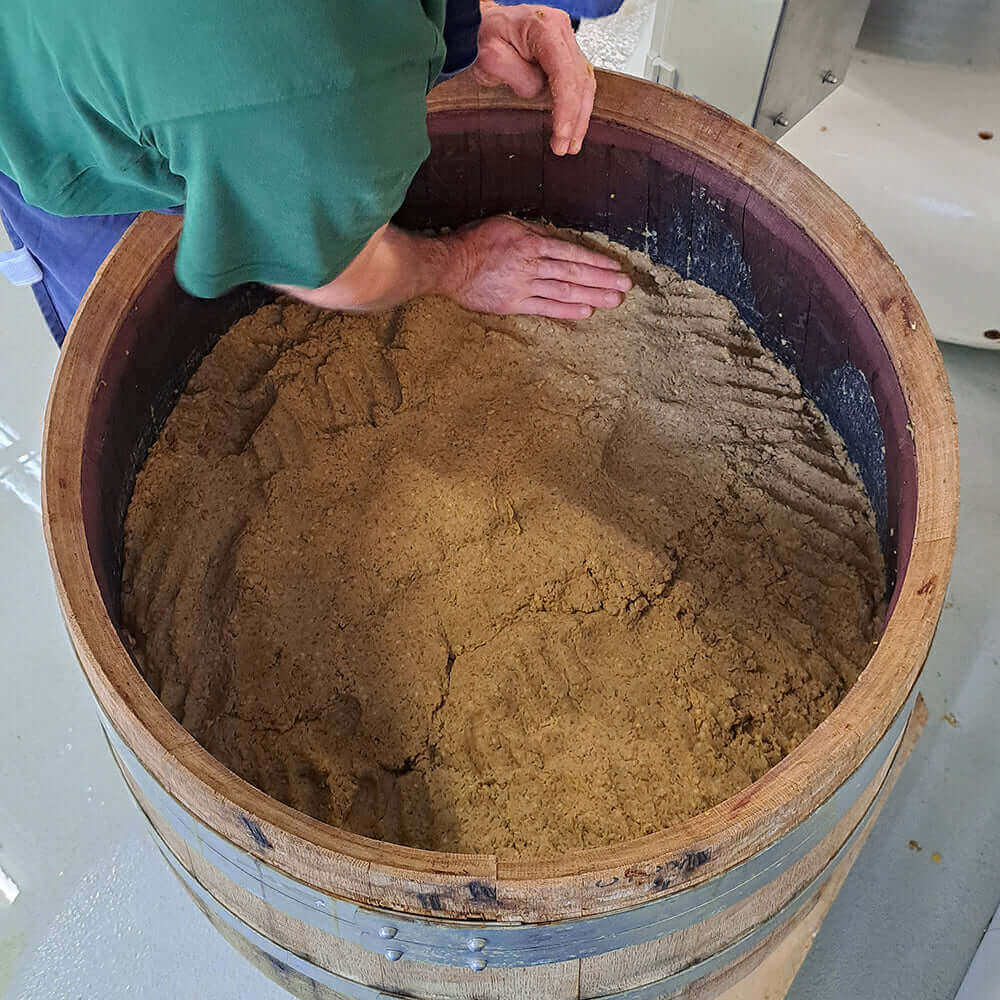 Ein Handwerker bearbeitet frisch zubereitete Miso Paste in einem Holzfass.